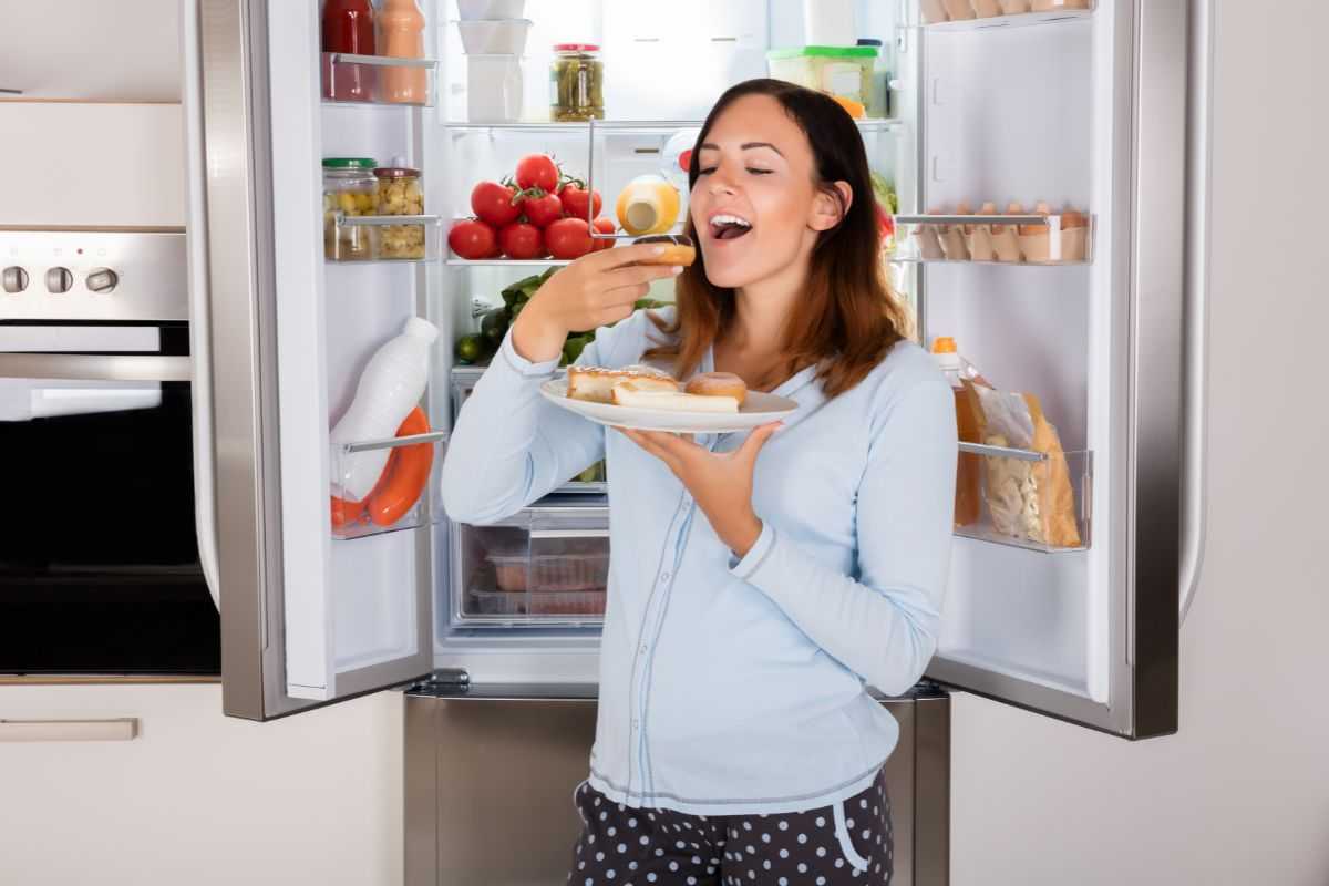 donna davanti al frigo che mangia un dolce